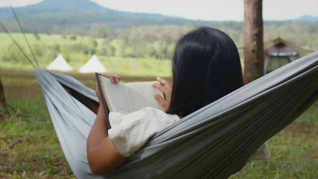 Asian woman lying down on hammock and reading a book