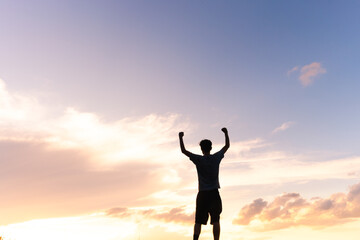 A silhouette of a man against the golden sunset sky, arms raised and fists clenched in a powerful...