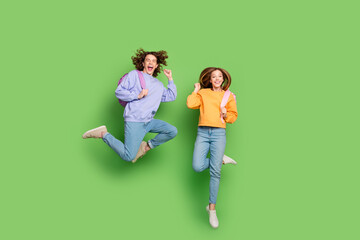 Full size photo of two excited cheerful people carry rucksack jump raise fists isolated on green...