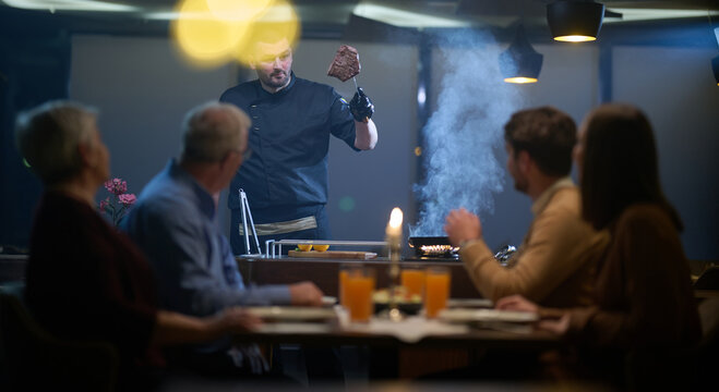 In a restaurant setting, a professional chef presents a sizzling steak cooked over an open flame, while an European Muslim family eagerly awaits their iftar meal during the holy month of Ramadan