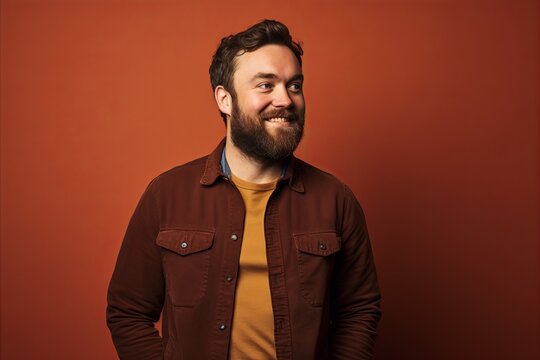 Portrait of a handsome bearded man in a brown jacket over red background.