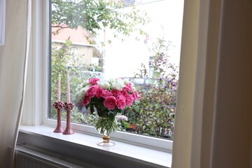 Vase with beautiful bouquet of roses and candles on windowsill indoors