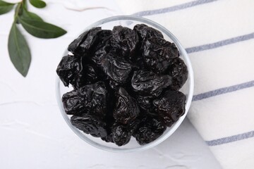Sweet dried prunes in bowl on white table, top view