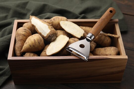 Tubers of turnip rooted chervil and peeler in wooden crate on table, closeup