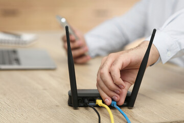 Man inserting cable into Wi-Fi router at wooden table indoors, closeup