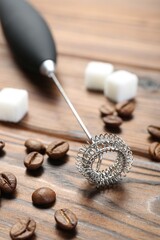 Black milk frother wand, sugar cubes and coffee beans on wooden table, closeup