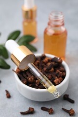 Clove oil in pipette and bowl with dried buds on grey table, closeup