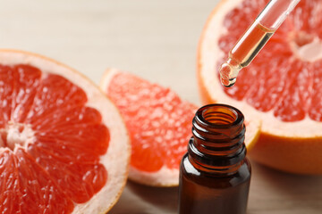 Grapefruit essential oil dripping from pipette into bottle and fresh fruits on light background,...