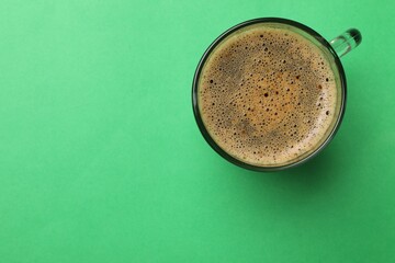 Aromatic coffee in glass cup on green background, top view. Space for text