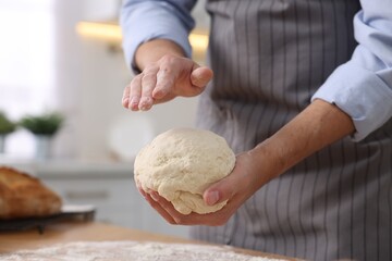 Making bread. Man kneading dough at wooden table in kitchen, closeup