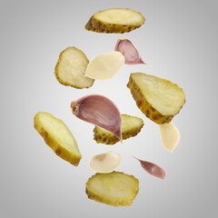 Slices of tasty pickled cucumbers and garlic falling on light grey background