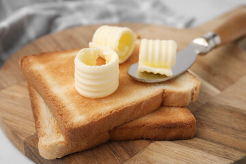 Tasty butter curls, knife and toasts on wooden board, closeup