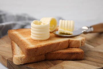 Tasty butter curls, knife and toasts on wooden board, closeup