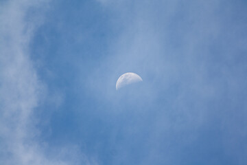 beautiful half moon in the day surrounded by wispy clouds in a blue sky