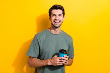Portrait of toothy beaming handsome guy with stubble holding takeaway cup of coffee in morning...