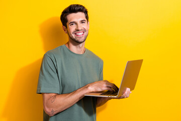 Portrait of clever cheerful guy with stubble wear stylish t-shirt typing message on laptop isolated on vivid yellow color background