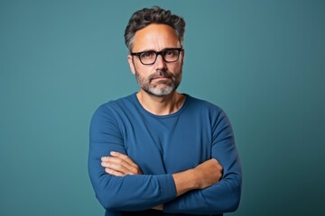 Handsome middle age man in blue sweater and eyeglasses looking at camera with arms crossed