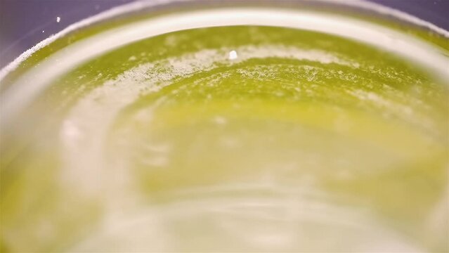 Top down view of viscous yellow liquid spinning along curved rim edge of glass, slow motion
