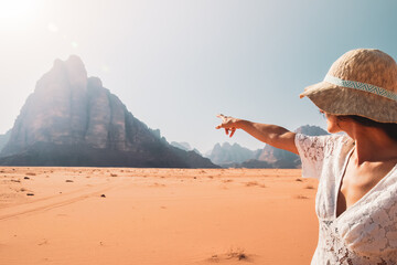 Back view female tourist stand watch point finger to seven pillars of wisdom monument in wadi rum...