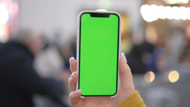 Use green screen for copy space closeup. Chroma key mock-up on smartphone in hand. Woman holds mobile phone and swipes photos or pictures in the mall 4K
