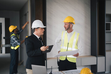 professional engineers in safety vests and hardhats working with blueprints and showing construction, Industrial engineers in hard hat discuss new project, they work in manufacturing factory.