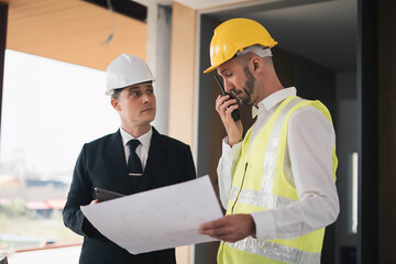 professional engineers in safety vests and hardhats working with blueprints and showing construction, Industrial engineers in hard hat discuss new project, they work in manufacturing factory.