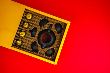 The concept of Asian tea, on a red background.Gift set for a traditional Chinese tea ceremony. Oolong milk tea in gold packaging. Japanese Tea set, cups and teapot with free space for text. 