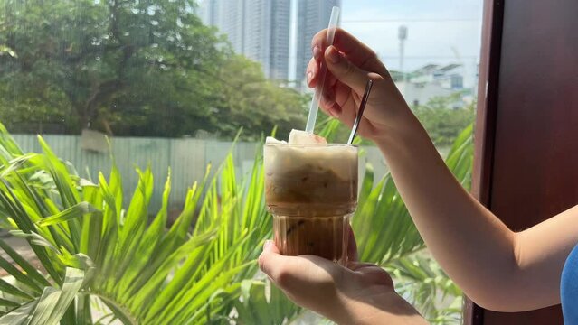 Traditional Vietnamese coffee with salt on the background of the window stir with a spoon thick white foam delicious a lot of condensed milk sweet coffee latte