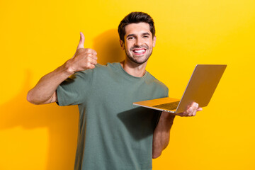 Portrait of toothy beaming guy with stubble wear stylish t-shirt hold laptop showing thumb up...