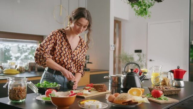 Woman at kitchen island with ingredients uses pestle and mortar to crush herbs