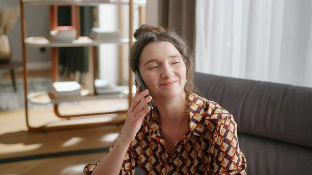 Close handheld shot of smiling woman talking on phone in living room