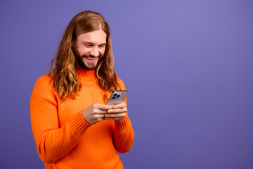 Closeup photo of young cheerful blond hair guy wearing orange sweater texting his friends hipsters isolated over purple color background