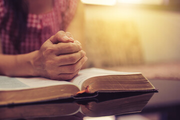 Close up of a woman hand  praying on  the open bible, blurred page on wooden table with window...
