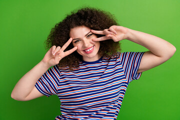 Photo of pretty positive lady toothy smile arms fingers demonstrate v-sign near eyes isolated on green color background