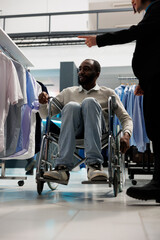 African american man in wheelchair pointing at shirt and asking consultant for advice while...