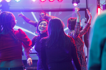 Happy diverse girlfriends partying and dancing at discotheque in nightclub. Cheerful smiling women...