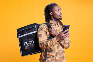 African american courier looking at customer address on smartphone takeout app before delivering...