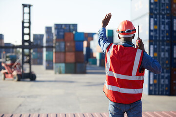 back view African factory worker or engineer using walkie talkie and showing stop gesture to crane...