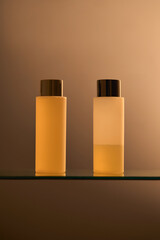 Two clear plastic cosmetic bottles with lids on glass stand. Shower gel, shampoo. Mockup, brand packaging, studio product photo. Minimalist luxury design.  Warm brown colored gradient backdrop, copysp - 731478062