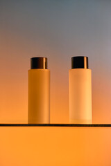 Two clear plastic cosmetic bottles with lids on glass stand. Shower gel, shampoo. Mockup, brand packaging, studio product photo. Minimalist luxury design. Orange blue gradient colorful backdrop. Copy 