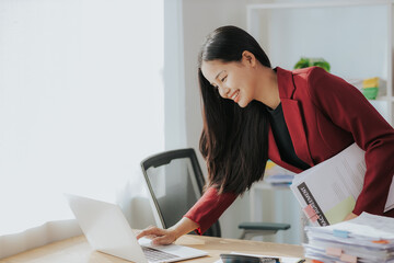 Cute Asian businesswoman in suit in modern workplace. Thai woman. Southeast Asian woman. looking at laptop in office