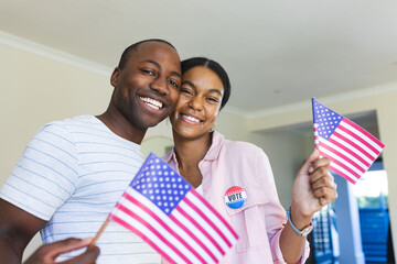 Young African American man and biracial woman holding flags at home, proudly displaying their 'I Vot