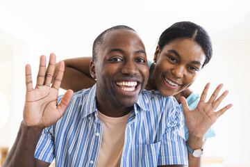 A young African American man and a biracial woman wave cheerfully during a video call on a smart hom