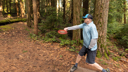 Wide shot of a man throwing a driver disc on a disc golf course on the Kitsap Peninsula