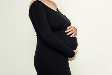 Pregnant woman in elegant dres holds hands on belly on a white background at studio. Pregnancy,...