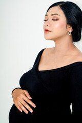 Obraz premium Pregnant woman in elegant dres holds hands on belly on a white background at studio. Pregnancy, maternity, preparation concept. Close-up, copy space, indoors.