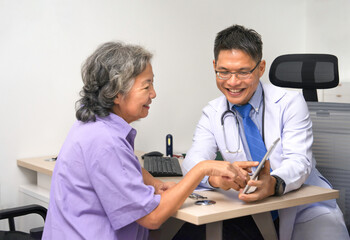 A mature medical professional male smiling and talking to senior woman patient in examine...