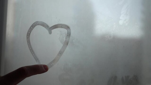 A finger draws a heart on a wet, foggy window. Joyful sign on glass in rainy weather