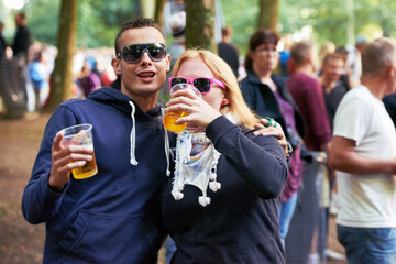 Drinks, happy and couple of friends at music festival, concert or party for outdoor rave or techno celebration. Portrait of young people, audience or crow in forest with beer or alcohol for holiday