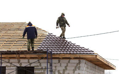 Workers install tiles on the roof of a house in winter